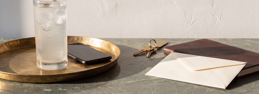 A concierge's working table in the afternoon, a brass tray and a glass of king coconut water beside a closed day book